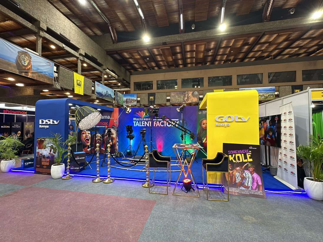 The same talent-factory stand seen down its length, screens lit along the run