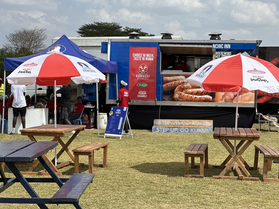 A Mobile Kenchic Inn unit open for service with food on the counter and branded umbrellas set up beside it