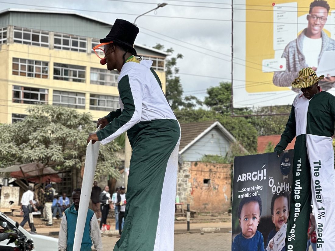 A stilt walker in costume carrying a printed placard above a street