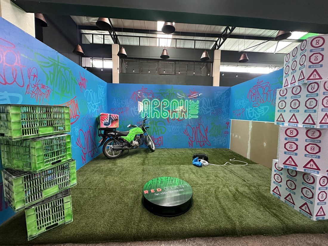 A built set dressed as an urban street corner with painted walls, stacked crates and a motorcycle on a turntable