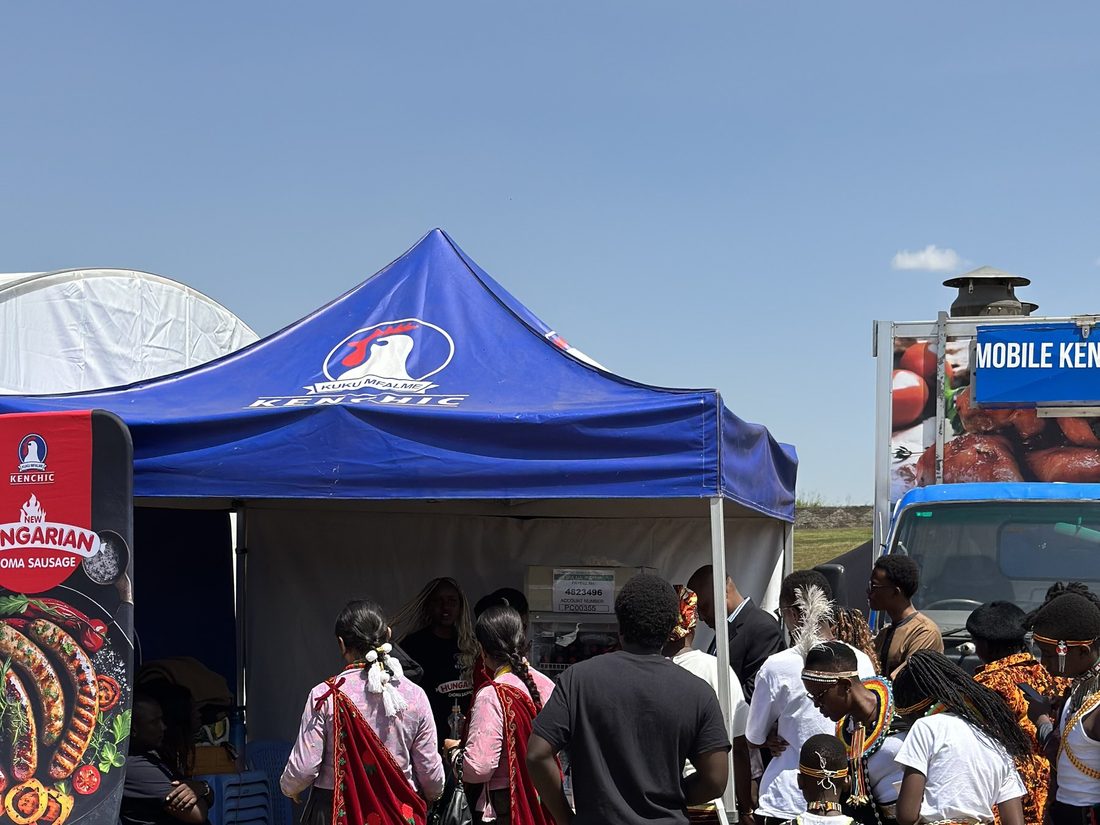 A crowd gathered on a lawn around performers in costume in front of a branded gazebo