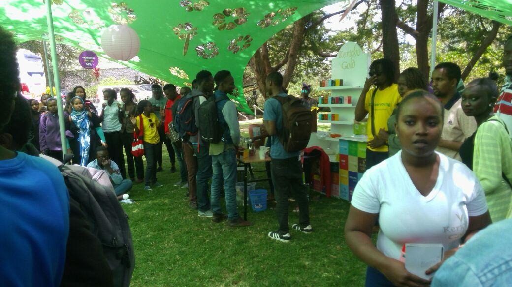 A branded merchandise shelf under a stretch tent with a dense student crowd in front of it
