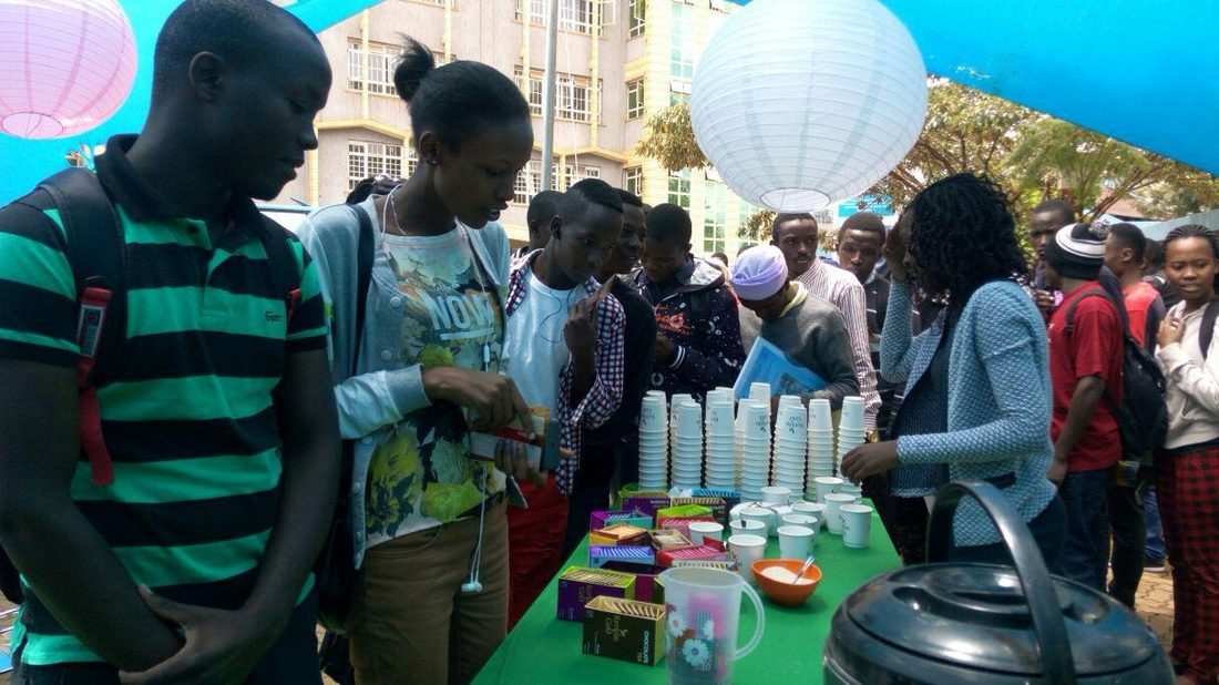 A crowd queuing at a sampling table on a campus lawn with a teaching block behind