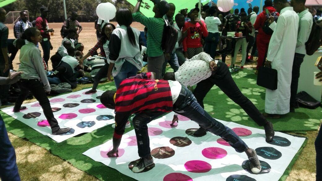 A wide view of students gathered around the Twister mat on a campus lawn
