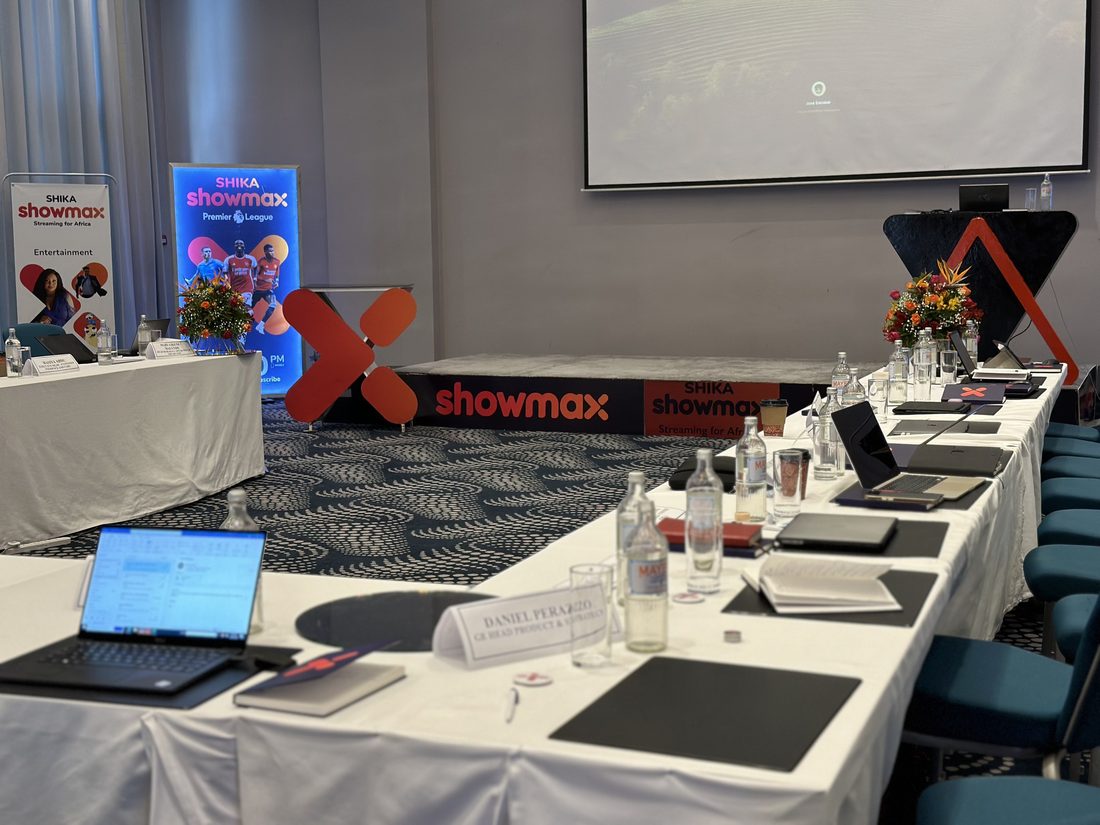 A boardroom table set with laptops and papers for a working session, with printed banners behind