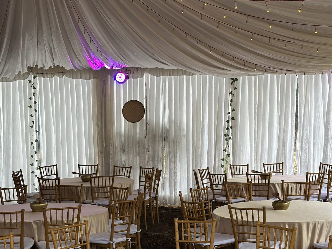 A draped marquee dressed with gold banquet chairs and round tables before guests arrive