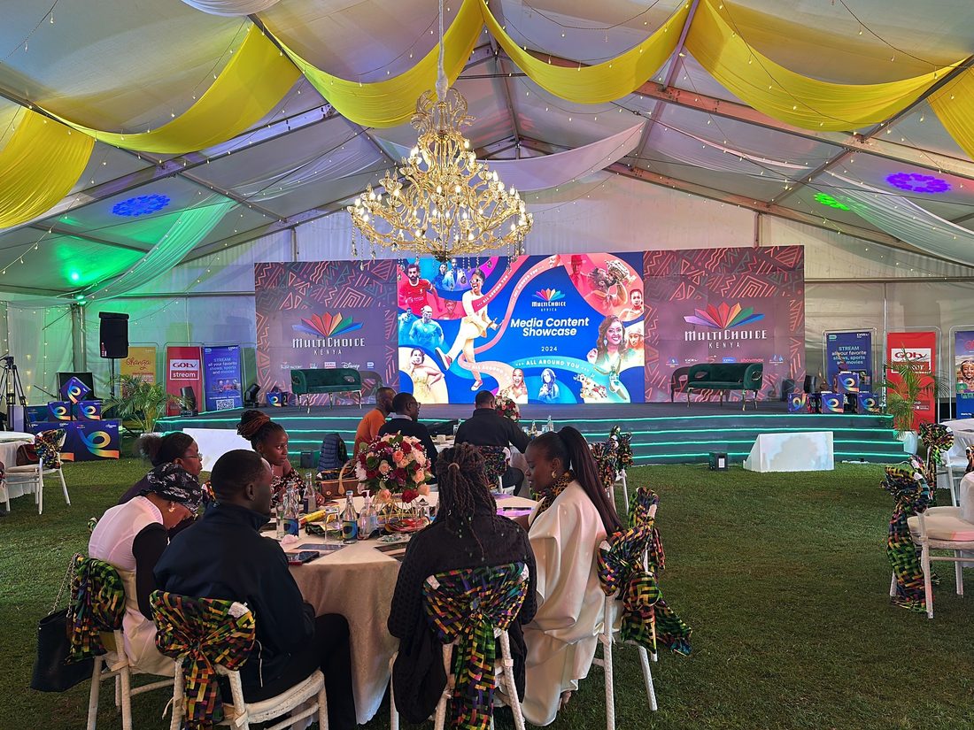 Guests seated at dressed tables inside a marquee facing an LED screen