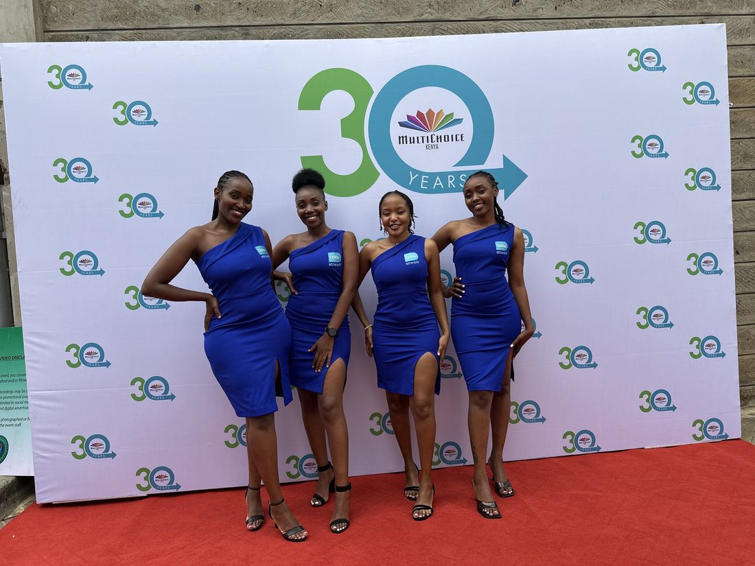 Four hostesses in matching dresses standing in front of a printed anniversary backdrop