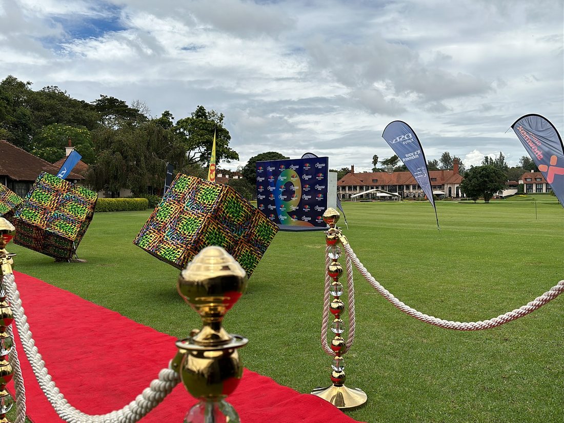 A red carpet run across a lawn flanked by gold rope stanchions and oversized printed gift cubes