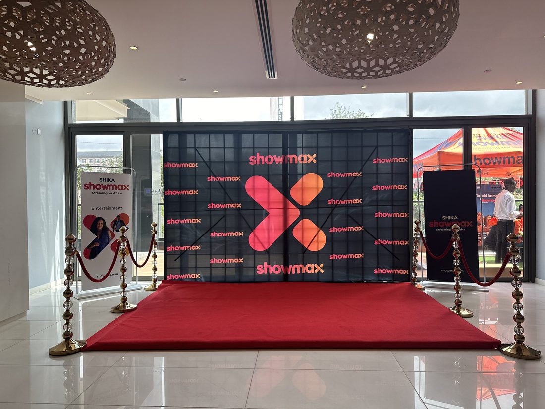 A red carpet and rope line leading to a sculptural brand installation in a lobby