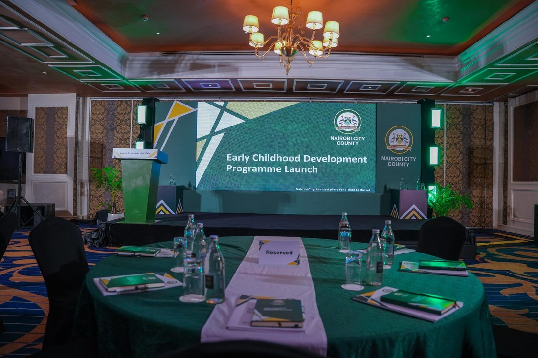 A round boardroom table set for a working session with a presentation on screen