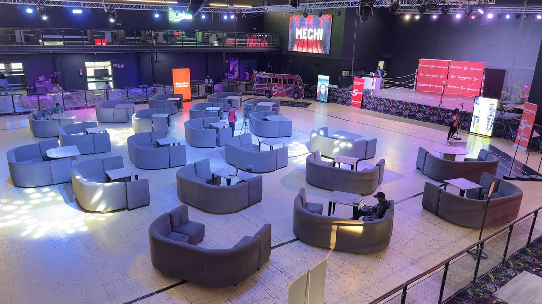 Curved lounge pods laid out across a venue floor in front of a stage, seen from the balcony