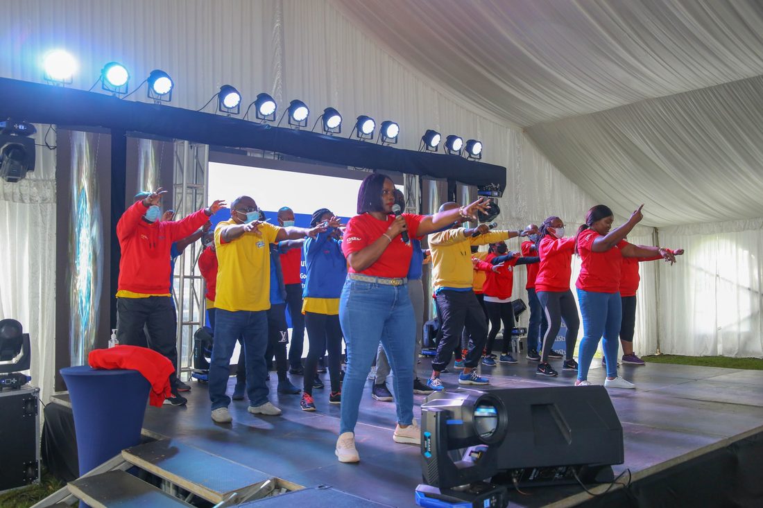 A group on stage under a lighting rig leading an energiser for the room