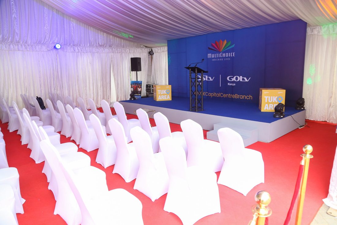 Rows of white-covered theatre seating either side of a red carpet aisle facing a branded stage