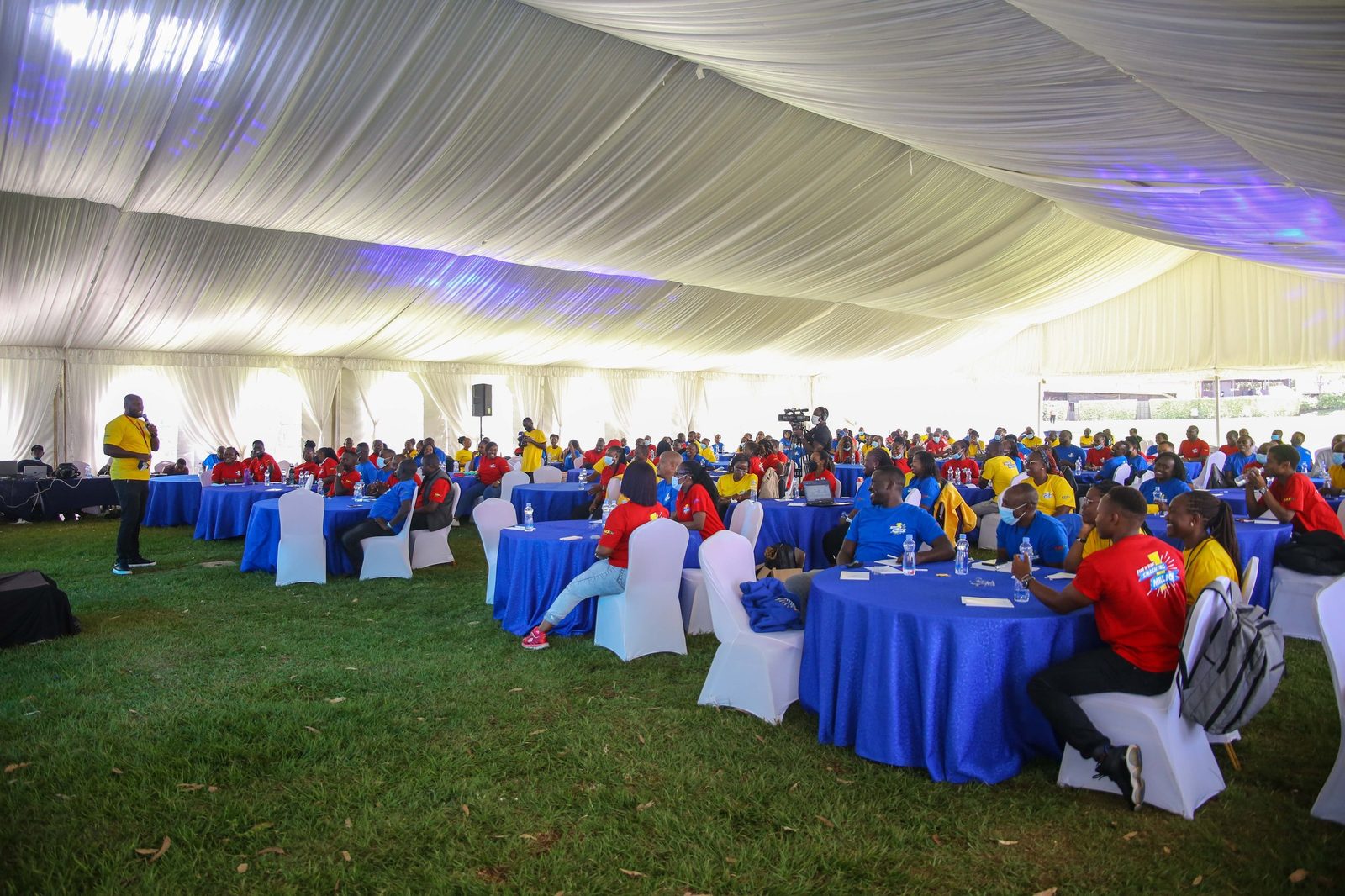 Delegates at dressed round tables under a marquee with a facilitator working the room