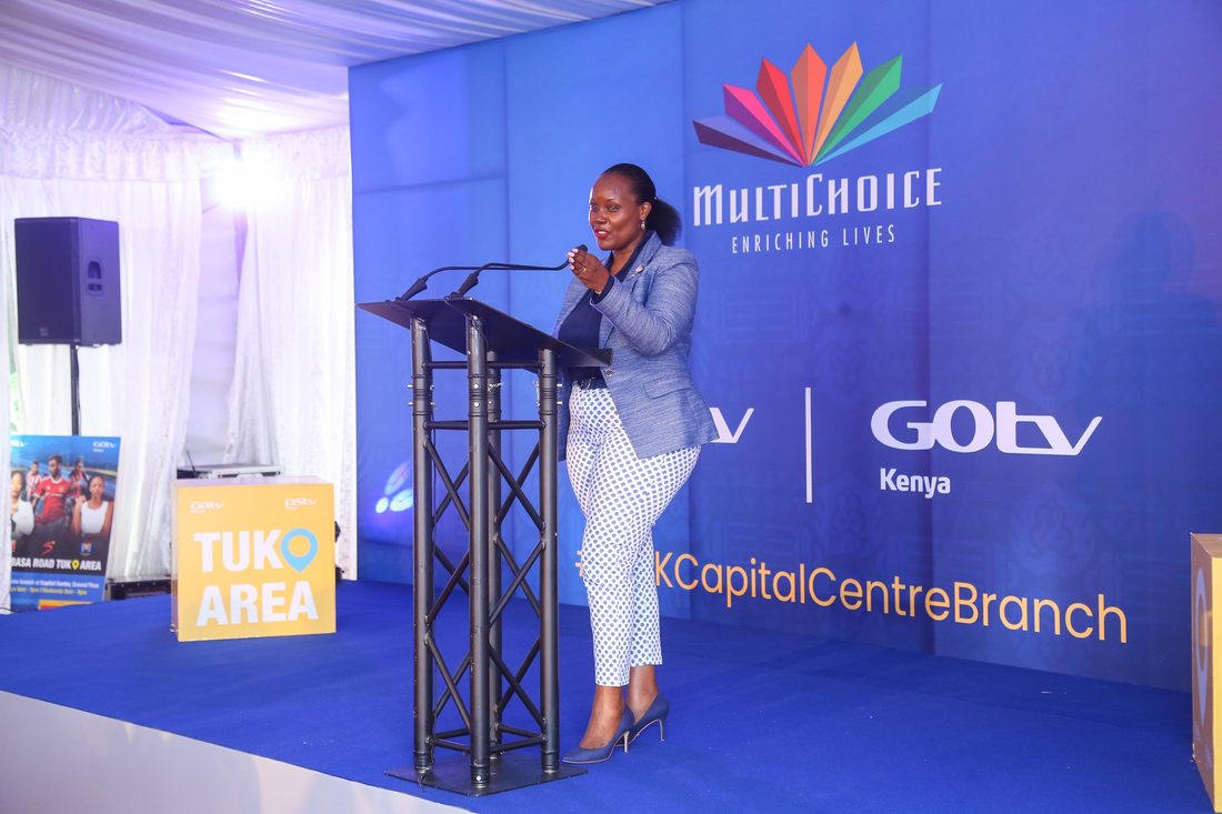 A speaker at a truss lectern in front of a clean branded backdrop