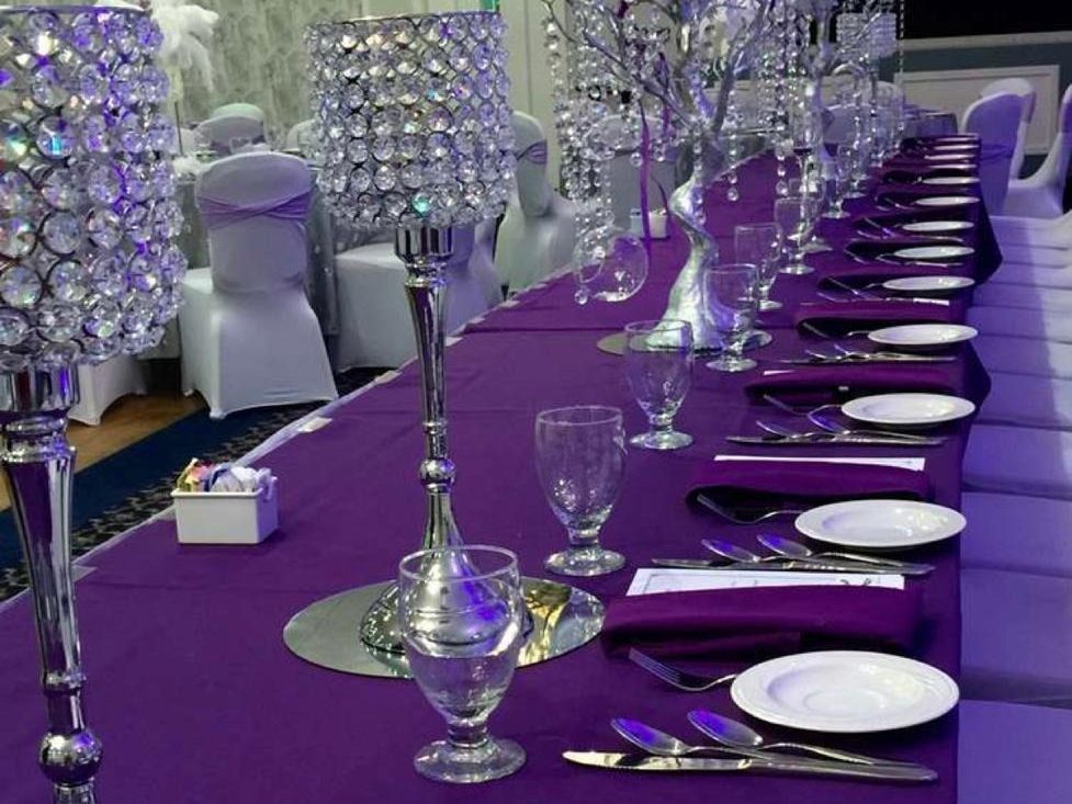 A long table dressed with a purple runner and full silver settings