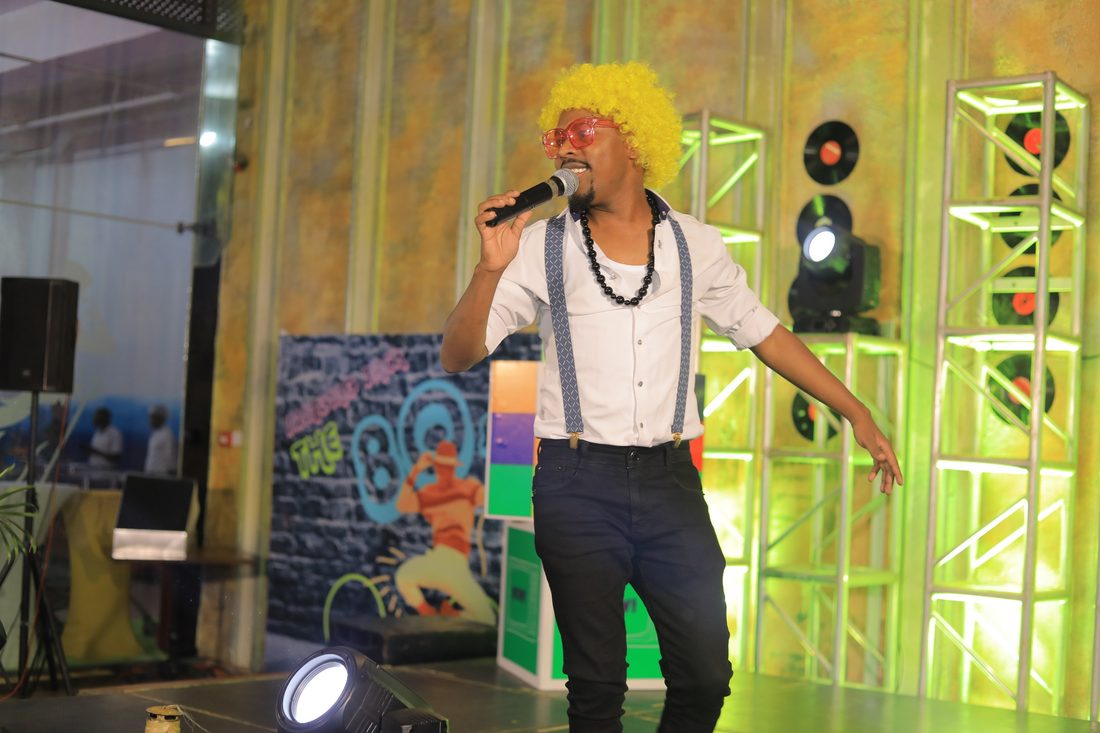 An MC in costume in front of a neon record-themed stage set