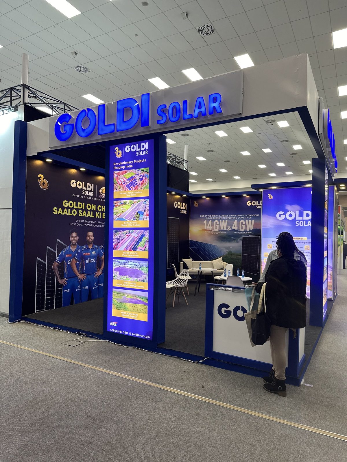 A Goldi Solar stand with illuminated lightbox towers and a visitor at the counter