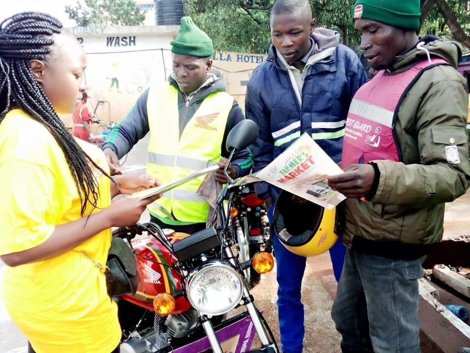 A promoter briefing three boda riders over a motorbike