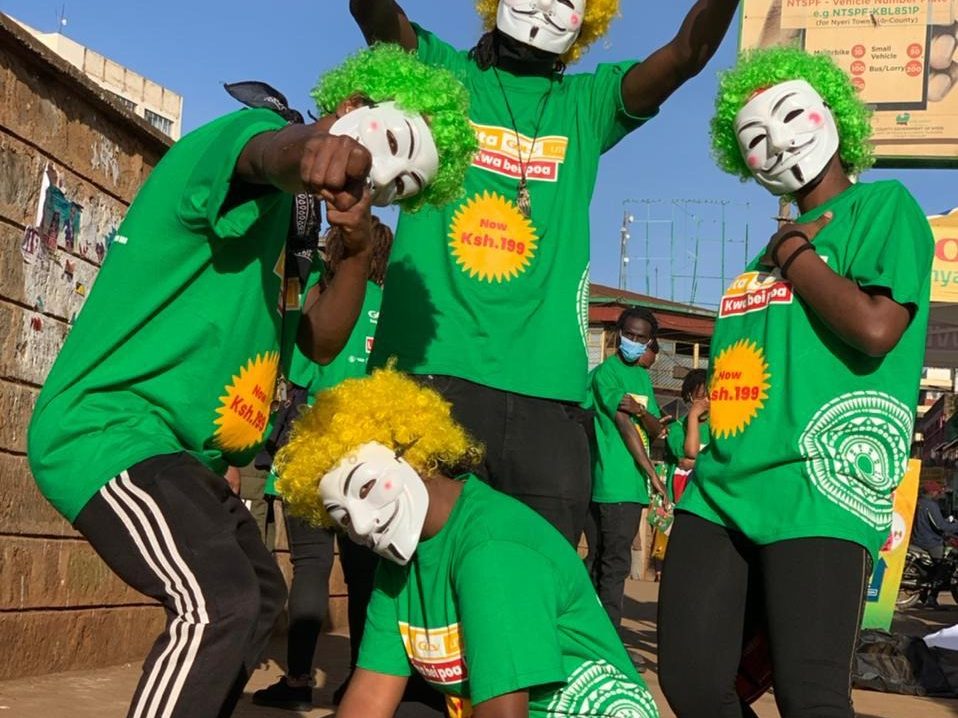 Costumed performers in green with masks and wigs on a street
