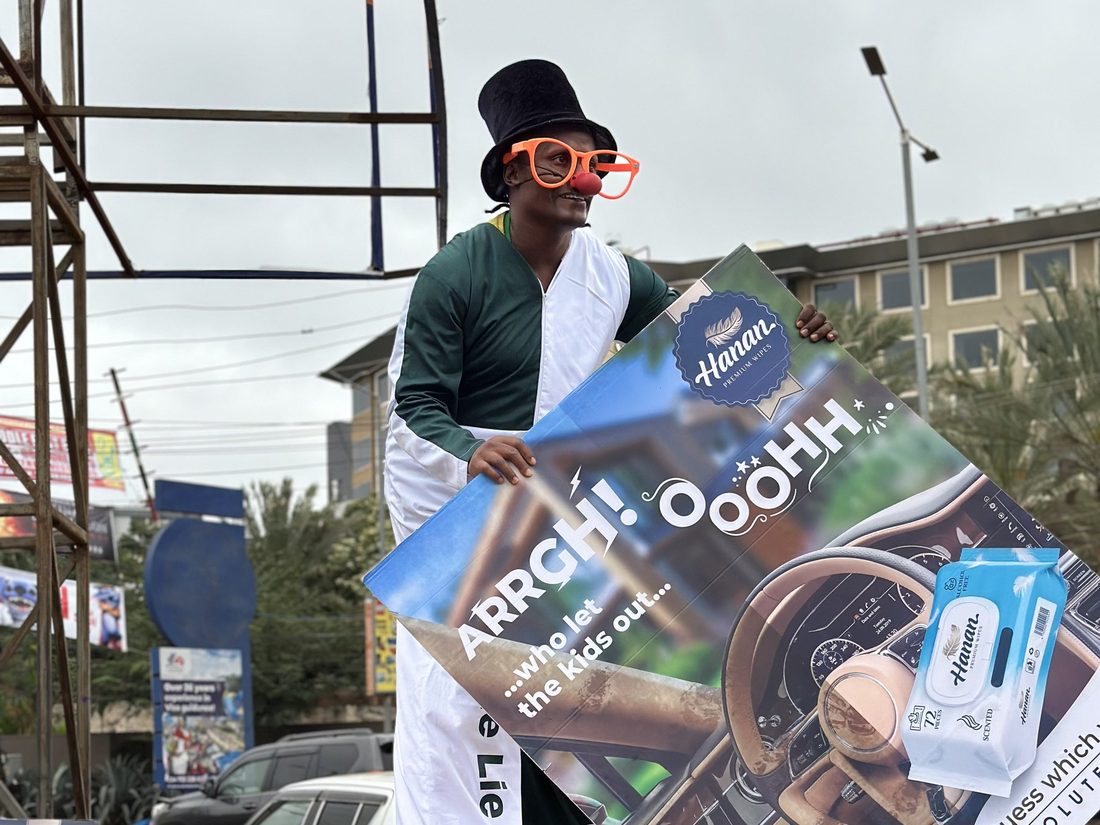 A stilt walker in costume carrying a branded flag along a street above the traffic