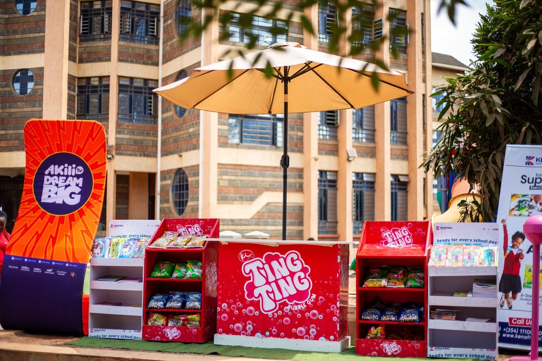 A branded retail unit with stocked shelves and a parasol on a paved forecourt