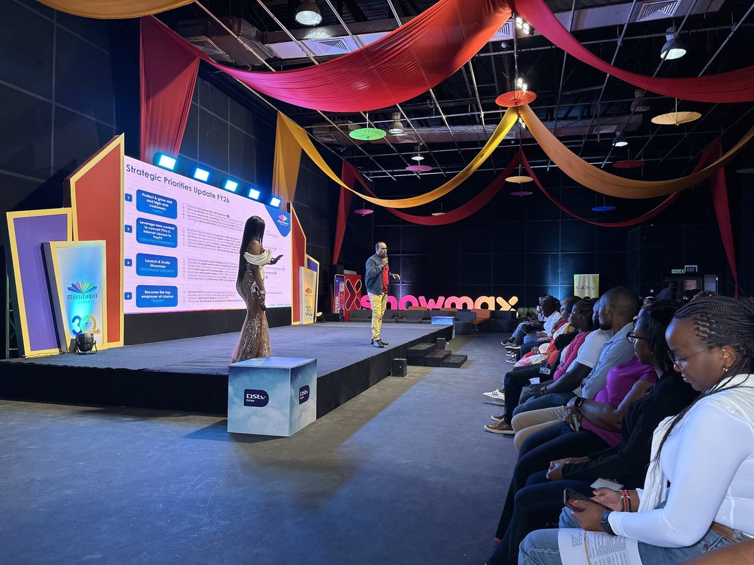 A runway stage with a seated audience alongside and a lit screen behind