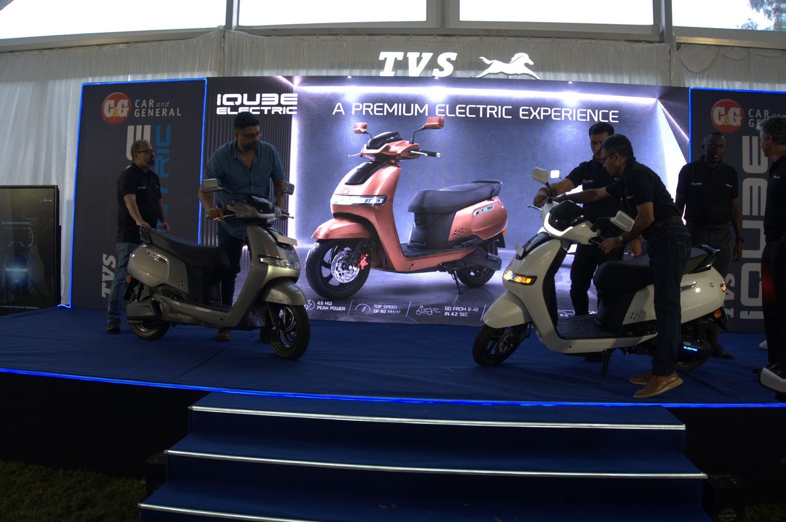 Two electric scooters presented on a lit stage under a printed header
