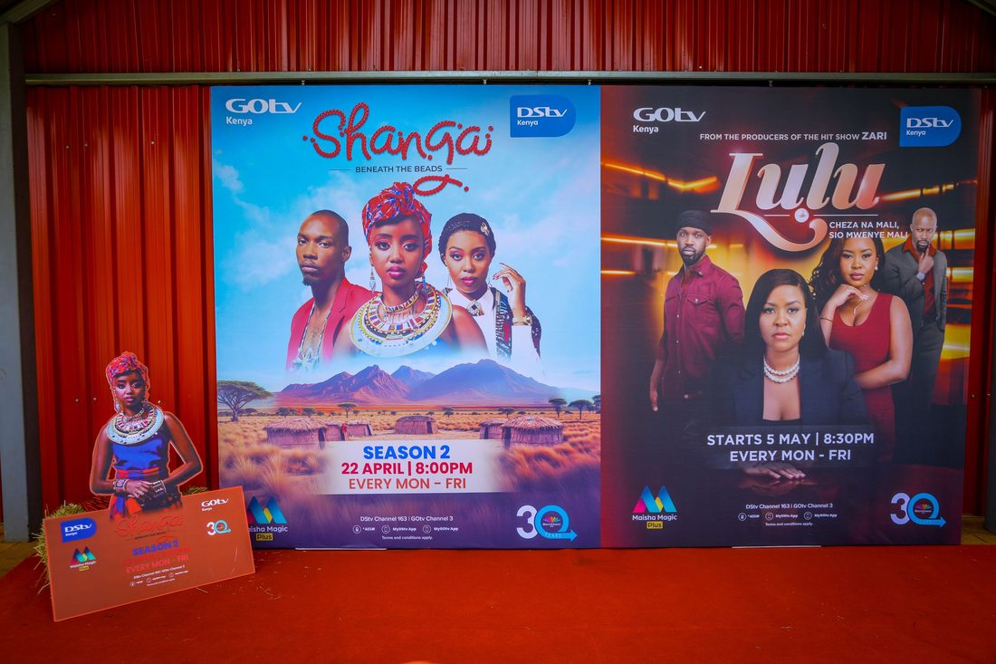 A launch backdrop carrying two series key visuals, set on a red carpet under a red drape