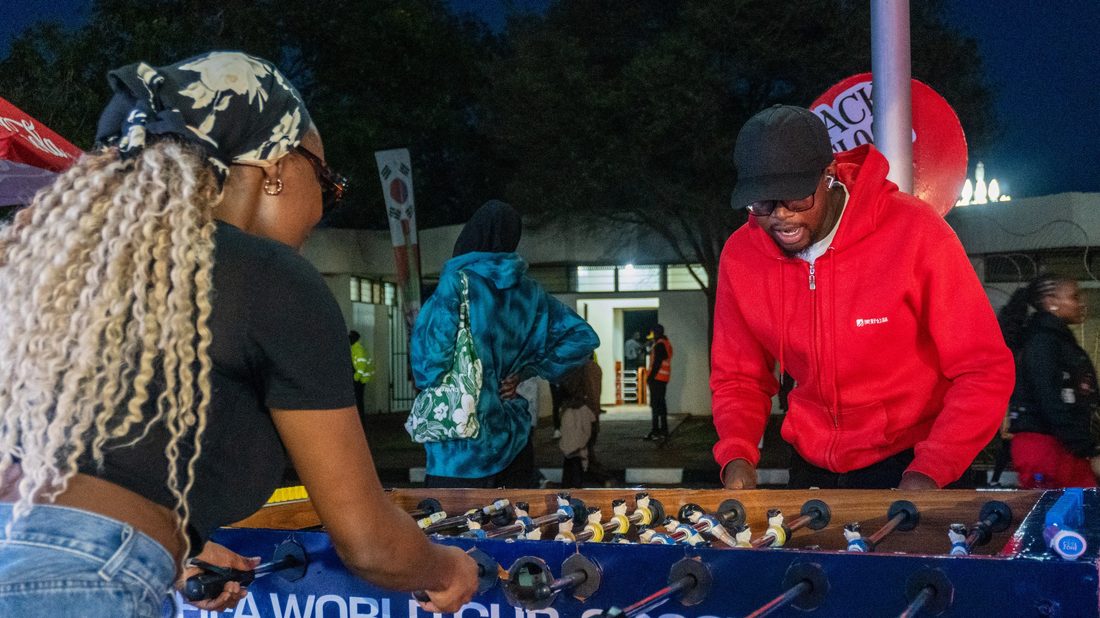 Two young adults playing a branded foosball table at dusk