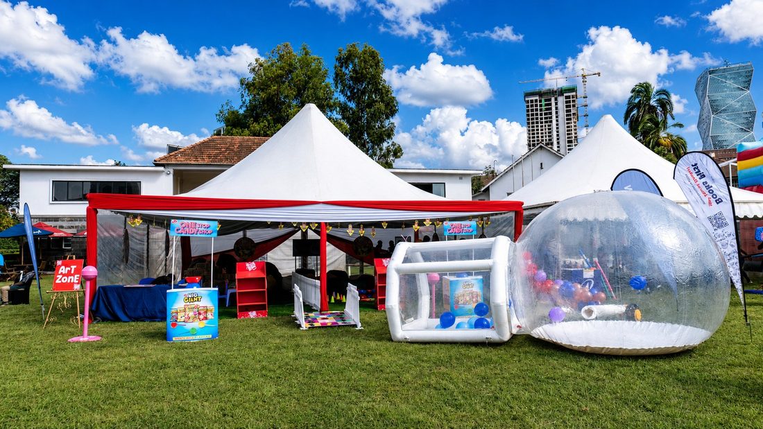 A garden pop-up with a red-draped marquee, a transparent bubble dome and a branded games area
