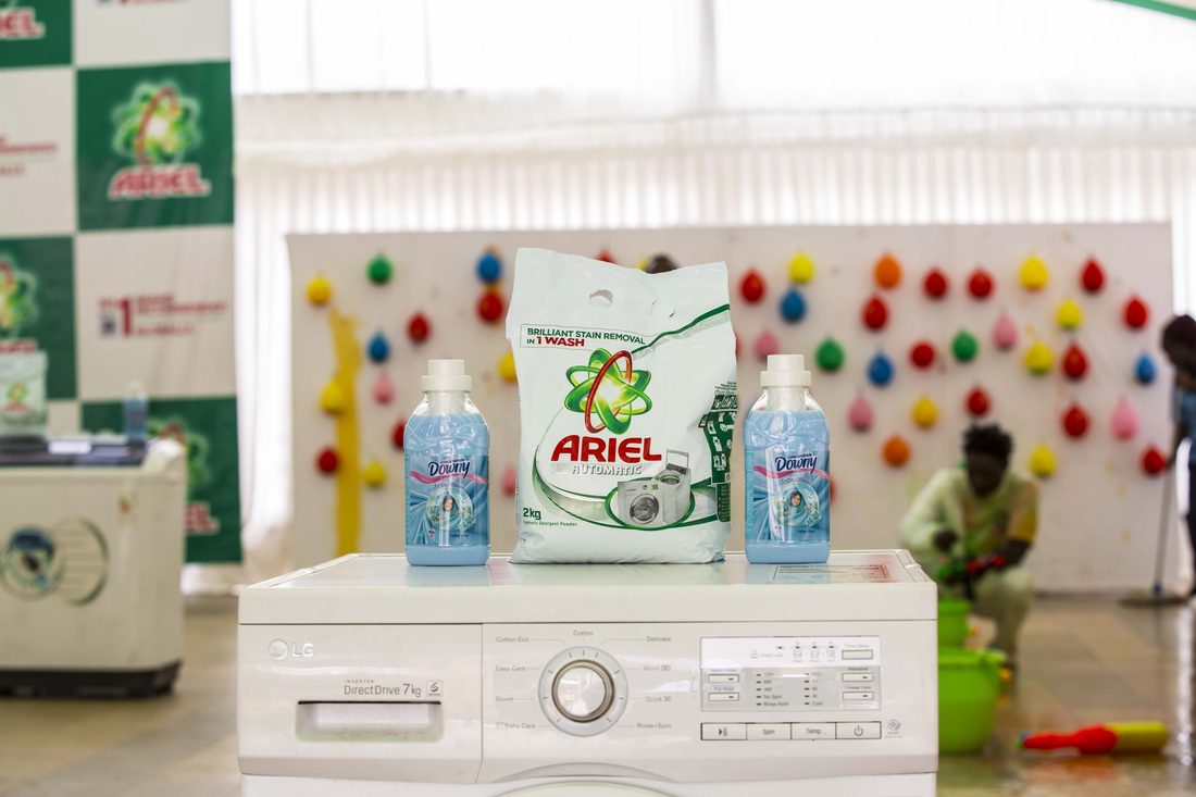 Ariel packs and bottles arranged on top of a washing machine against a colour-dotted backdrop