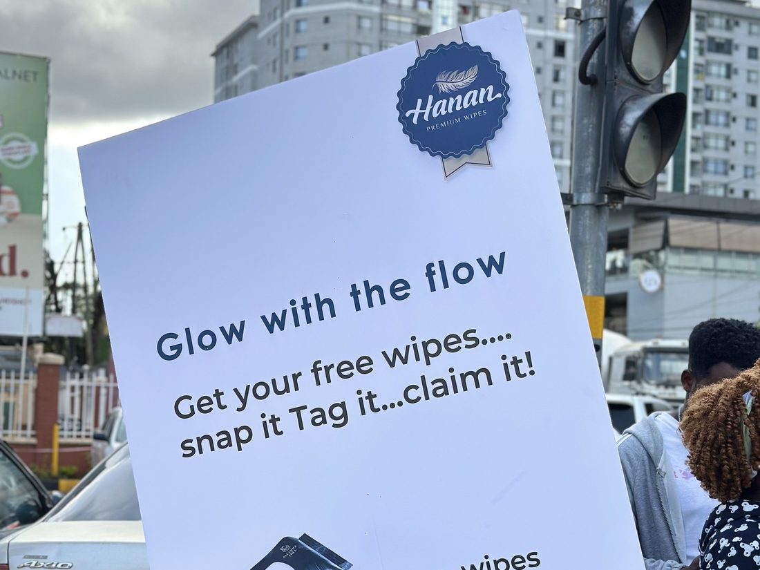 A promoter holding a Hanan sampling card at a road junction with pedestrians behind