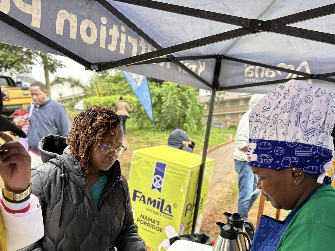 Two staff working an outdoor sampling stand, one holding a product carton