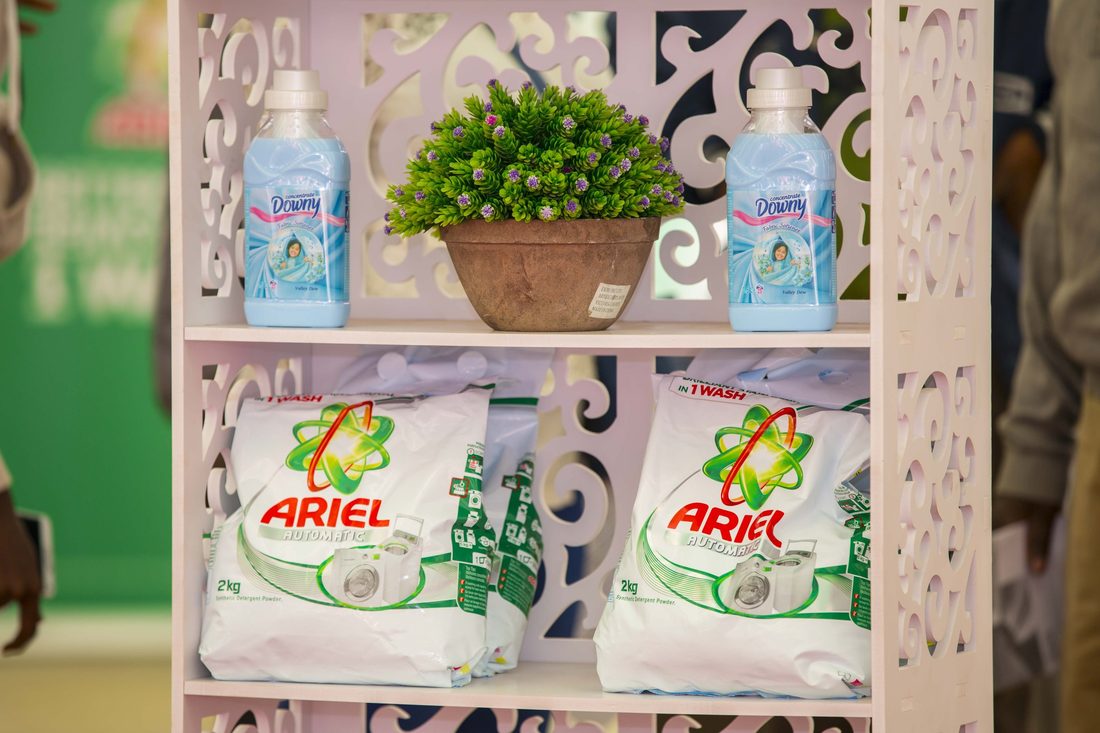 A merchandised shelf of Ariel packs and bottles dressed with greenery, shot close with a shallow depth of field