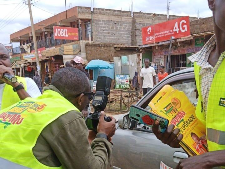 A hi-vis field crew handing a product pack to a passer-by beside a vehicle
