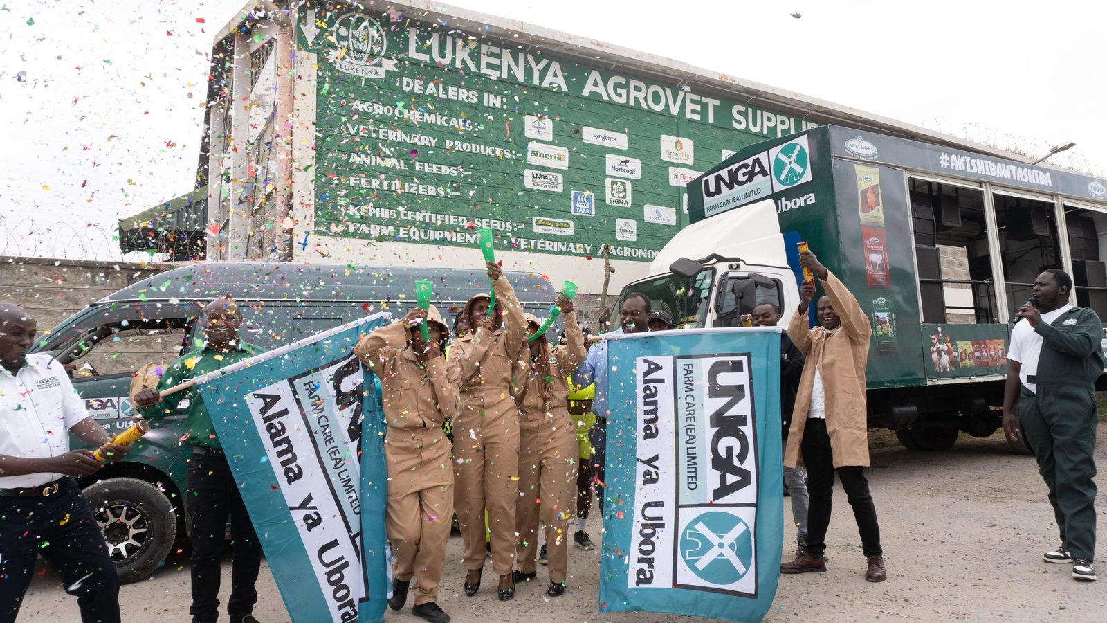 An Unga Farm Care route truck being flagged off at an agrovet, confetti cannons firing, uniformed field team and an MC on the microphone