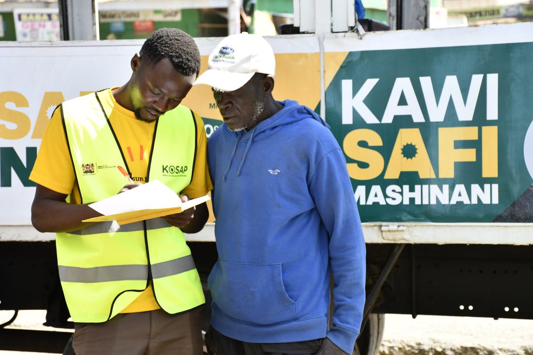 A field officer in a hi-vis vest completing a form with an older customer at the side of a roadshow truck