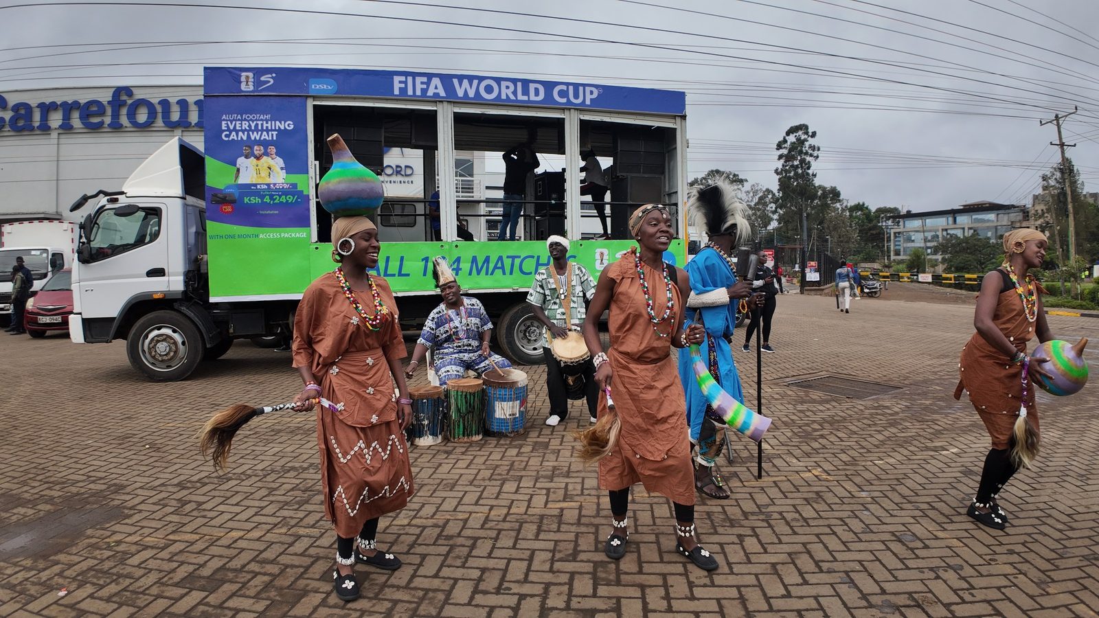 A branded roadshow truck parked outside a supermarket with a dance troupe performing in front of the stage bay while crew rig the side