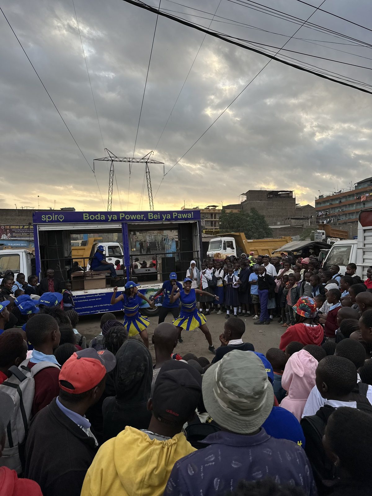 A large crowd gathered around a lit roadshow truck at dusk