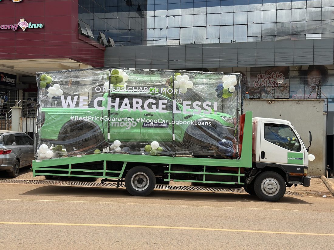 A Mogo branded truck dressed with balloons parked outside a row of shops
