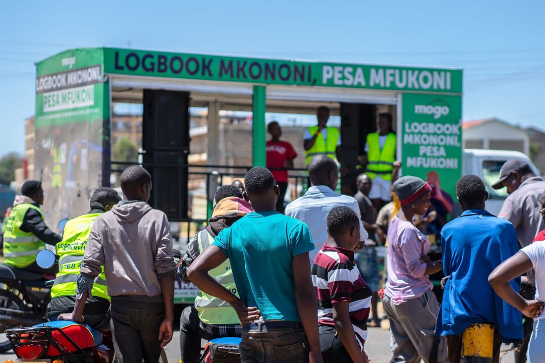 A crowd of boda riders and hi-vis crew in front of a Mogo branded truck