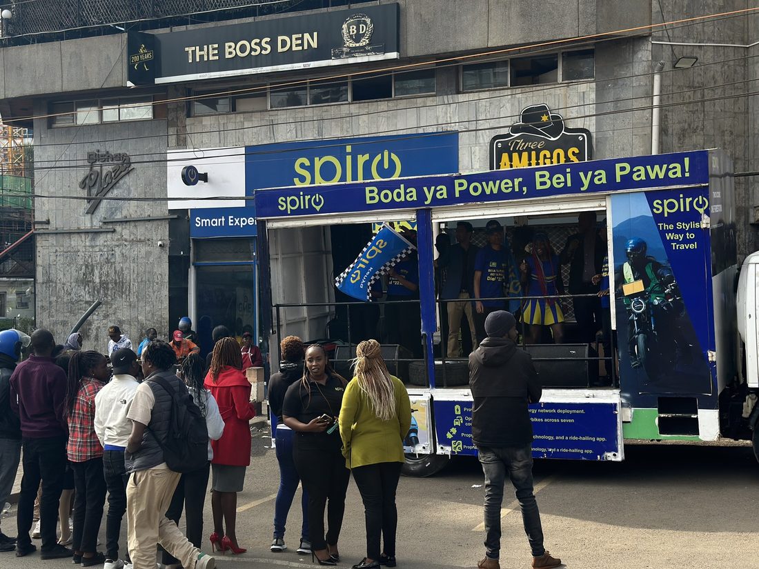 A Spiro branded truck parked outside a shopfront with a crowd of passers-by standing in front of the open stage bay