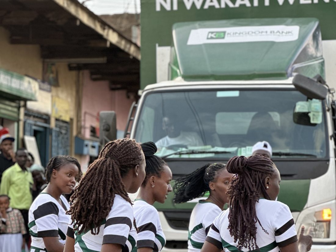 A dance troupe in matching green and white uniforms performing in the street beside a branded truck