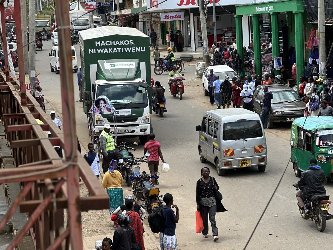 A branded roadshow truck moving through a busy town street lined with shops