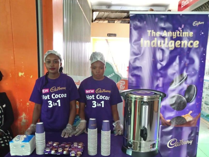 A hot cocoa sampling table with promoters in hairnets and gloves working beside an urn