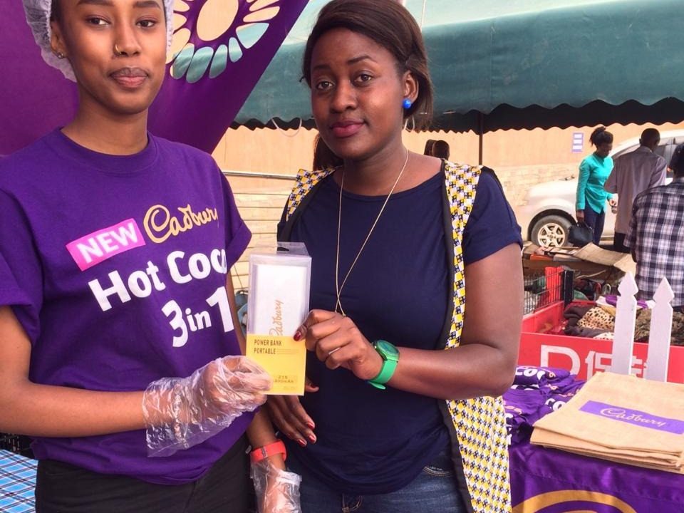A sample cup handed over against a branded backdrop