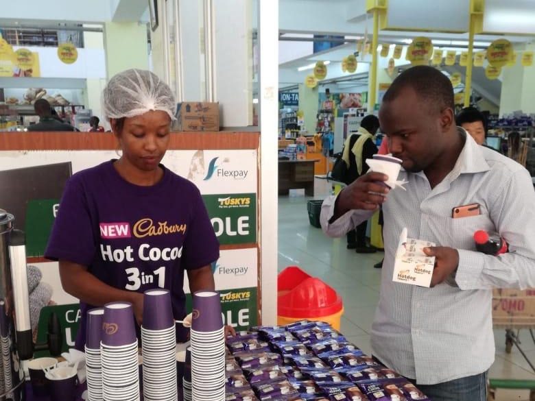 A consumer tasting a sample beside stacked product cartons