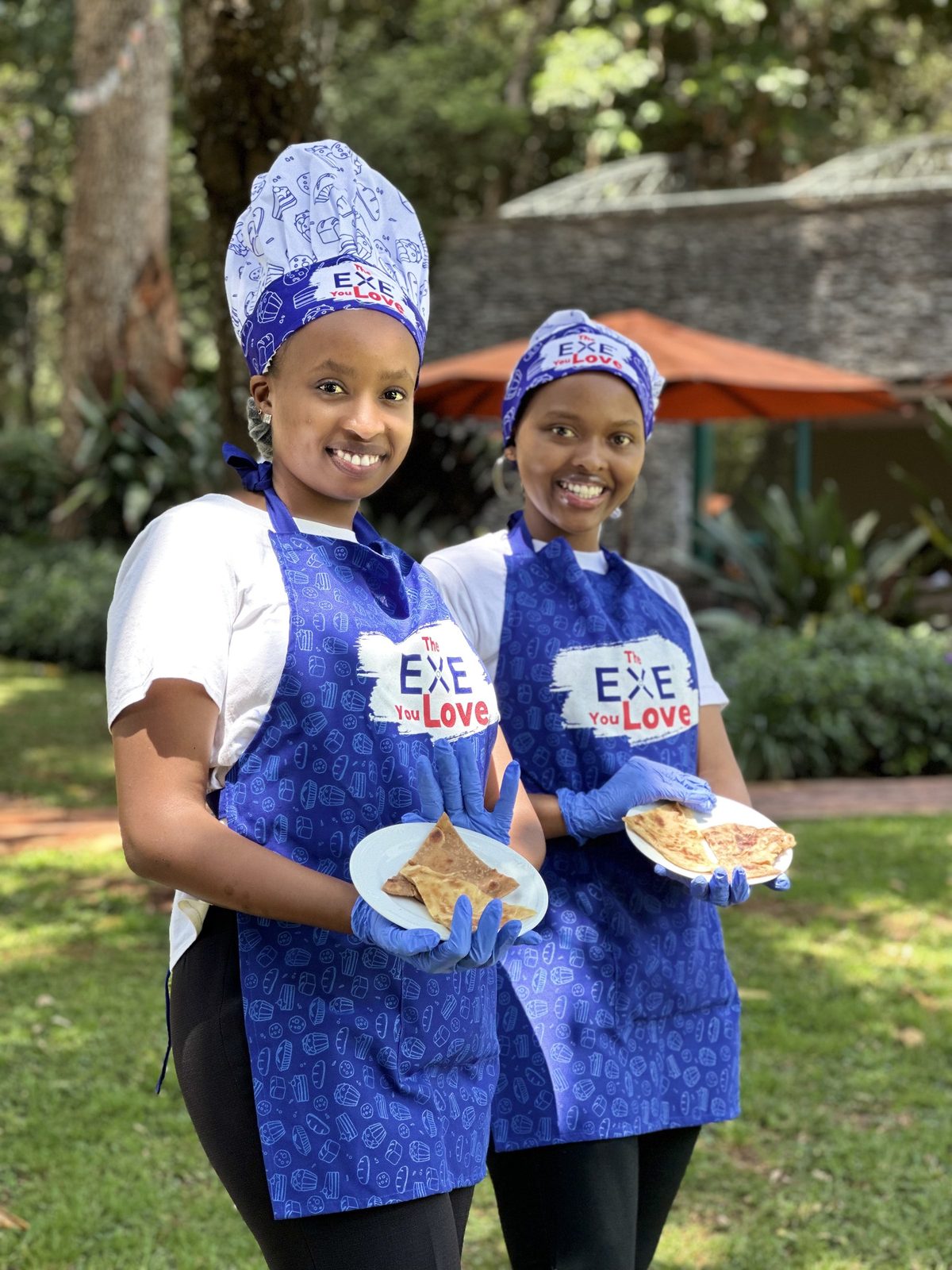 Two staff in branded aprons and headscarves holding plated product